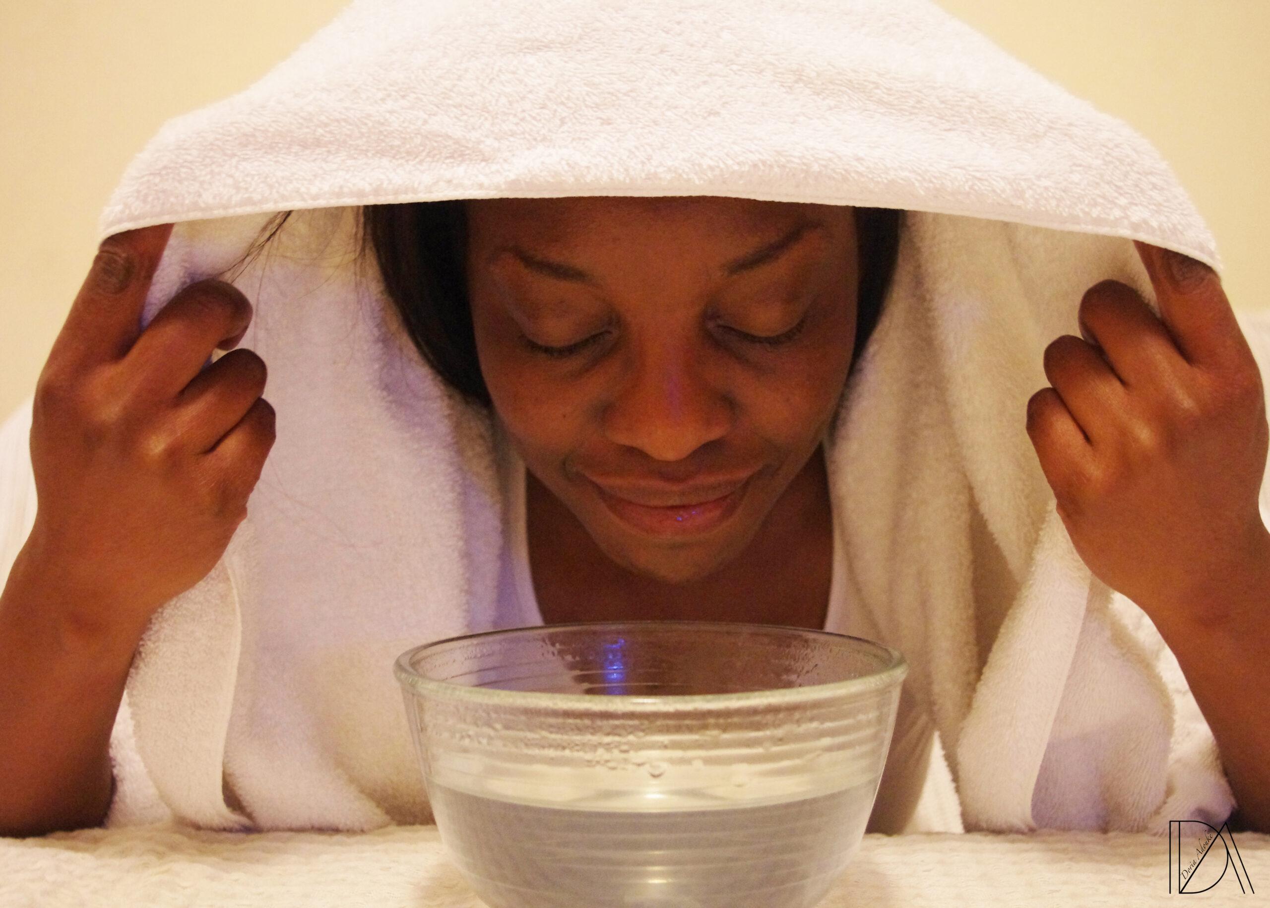A woman is steaming her face with a towel over her head.