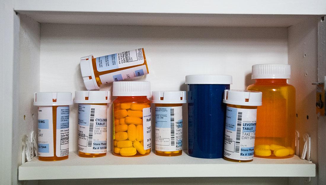A variety of prescription pill bottles sit on a white shelf.