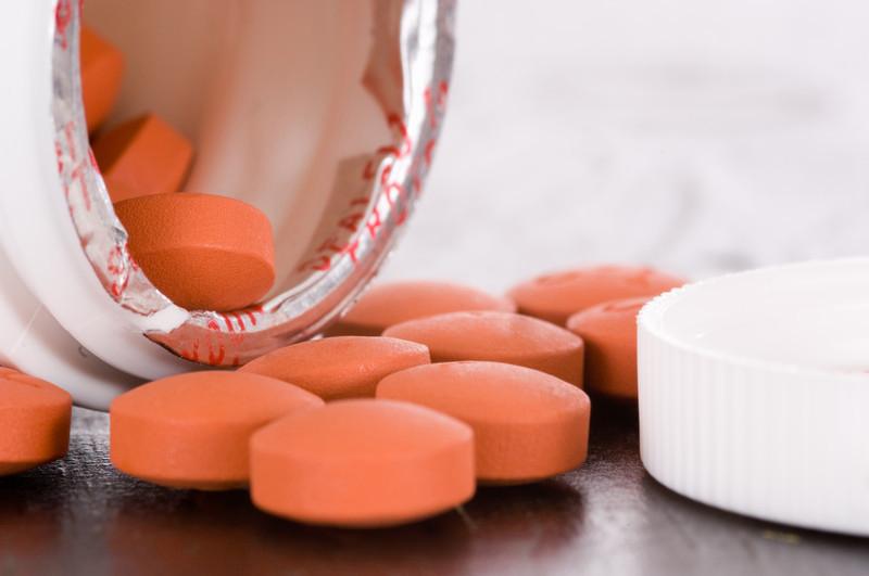Several orange pills spilled out of a white prescription bottle.