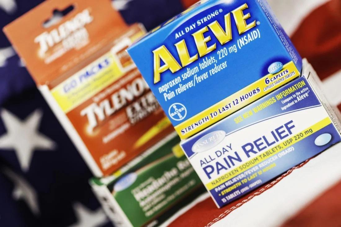 A variety of over-the-counter pain relievers are displayed in front of an American flag.