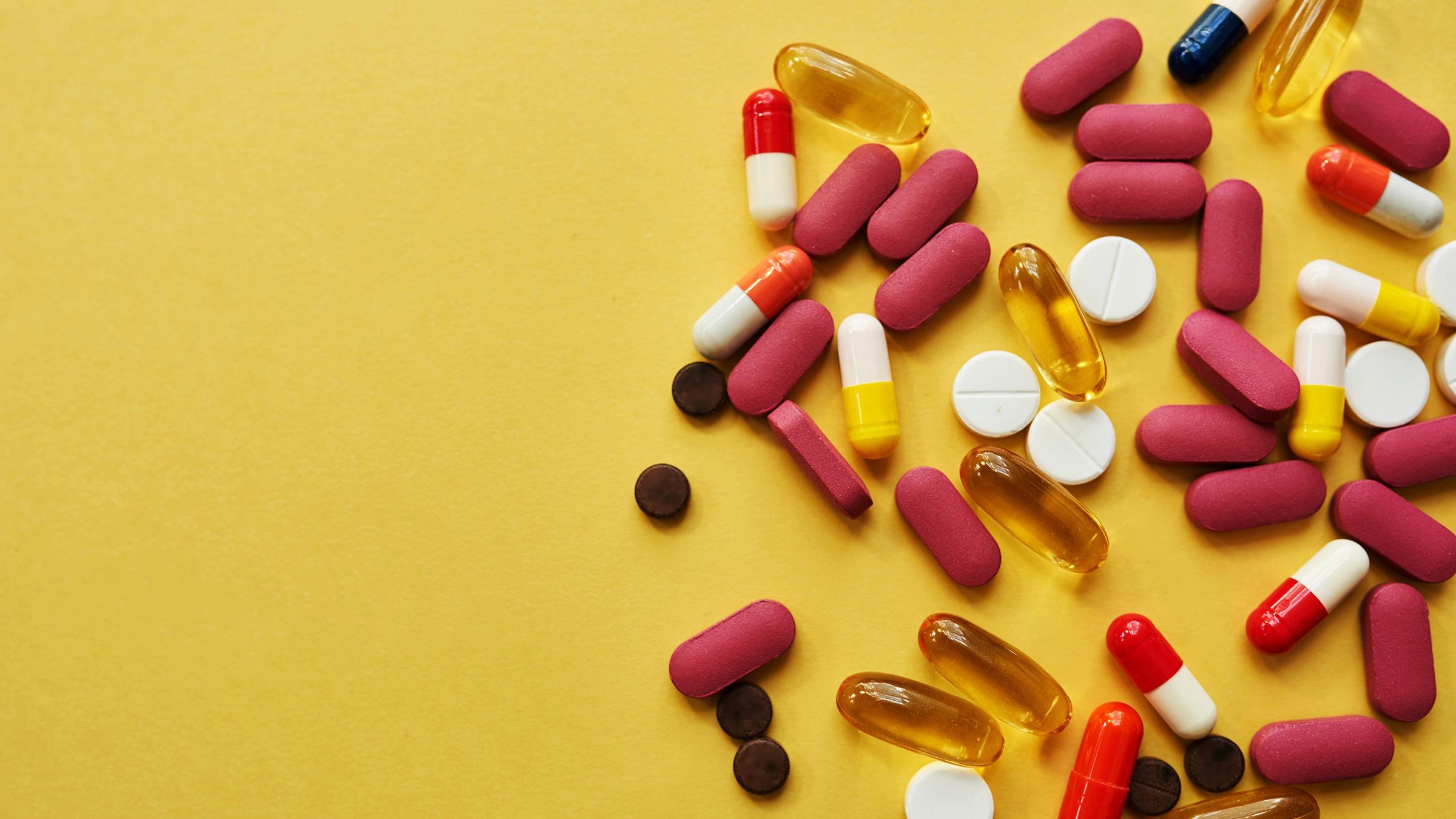 A flat lay of various pills and capsules on a yellow background.