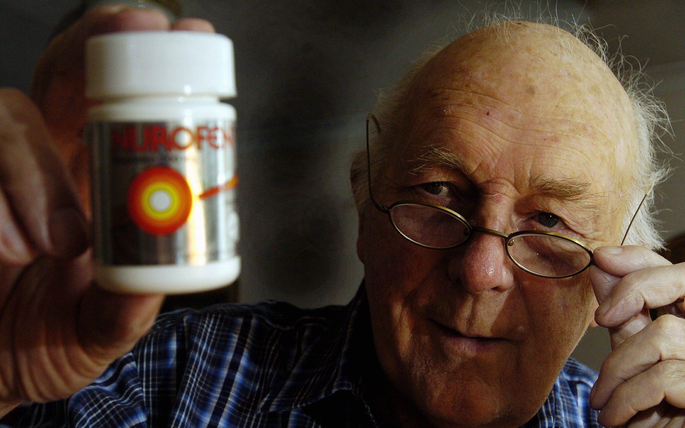 An elderly man holds up a bottle of Nurofen painkillers.