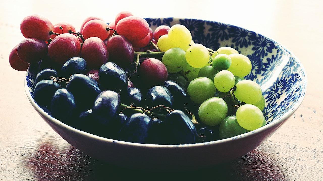 A bowl of red, green, and black grapes.