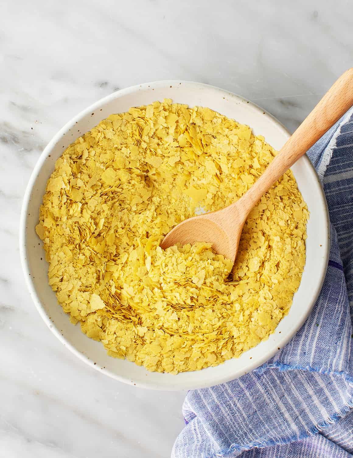 An overhead view of a bowl of nutritional yeast flakes with a wooden spoon.