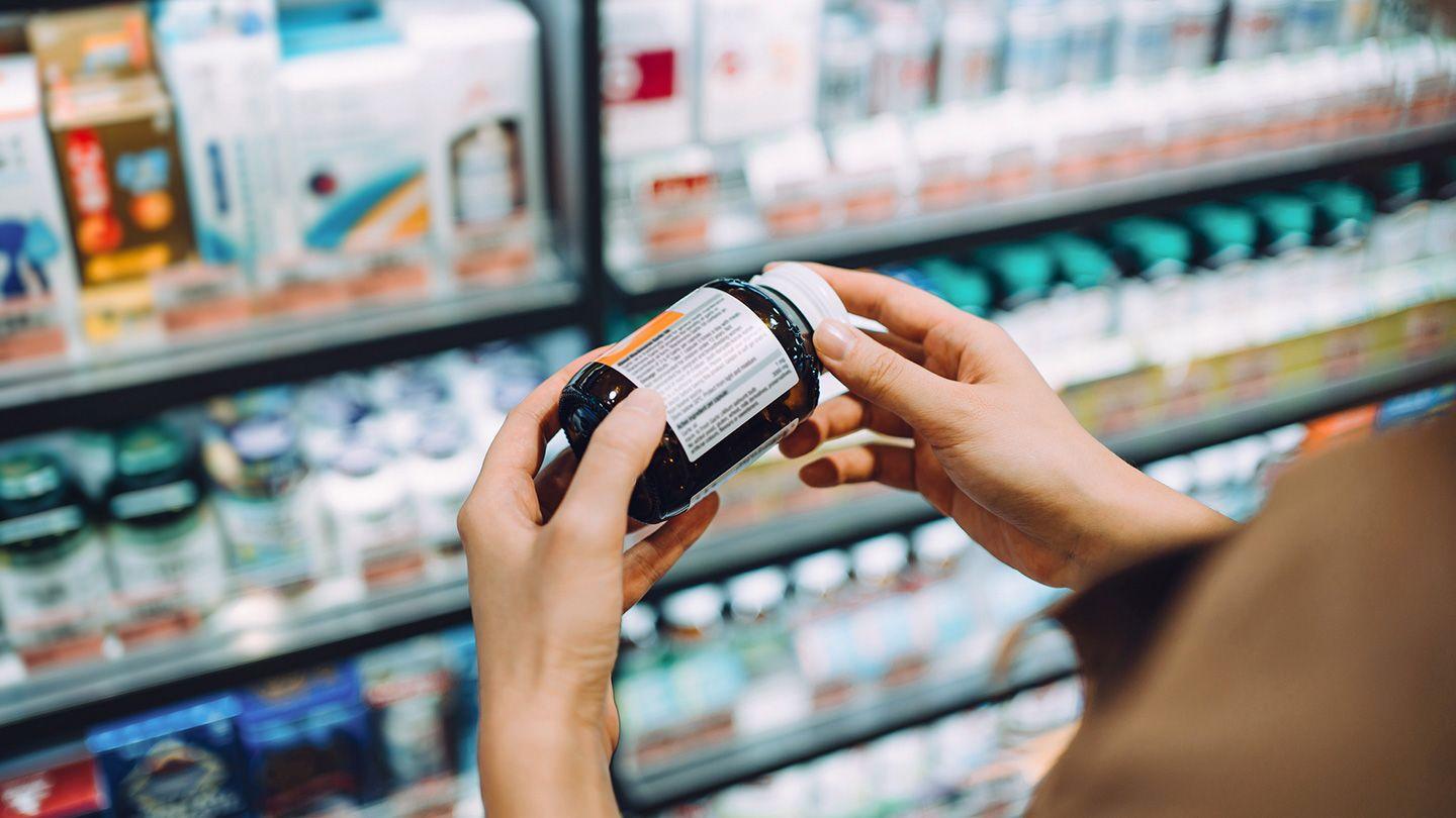 A woman is holding a bottle of pills in a drugstore and looking at the label.