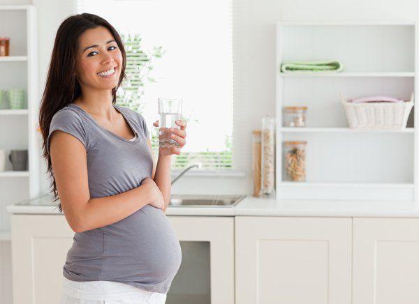 Pregnant woman drinking a glass of water in the kitchen.