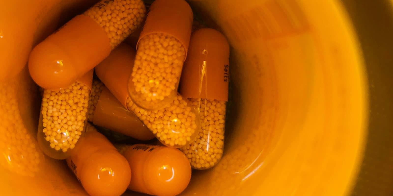 Several orange pill capsules sit in an orange container.