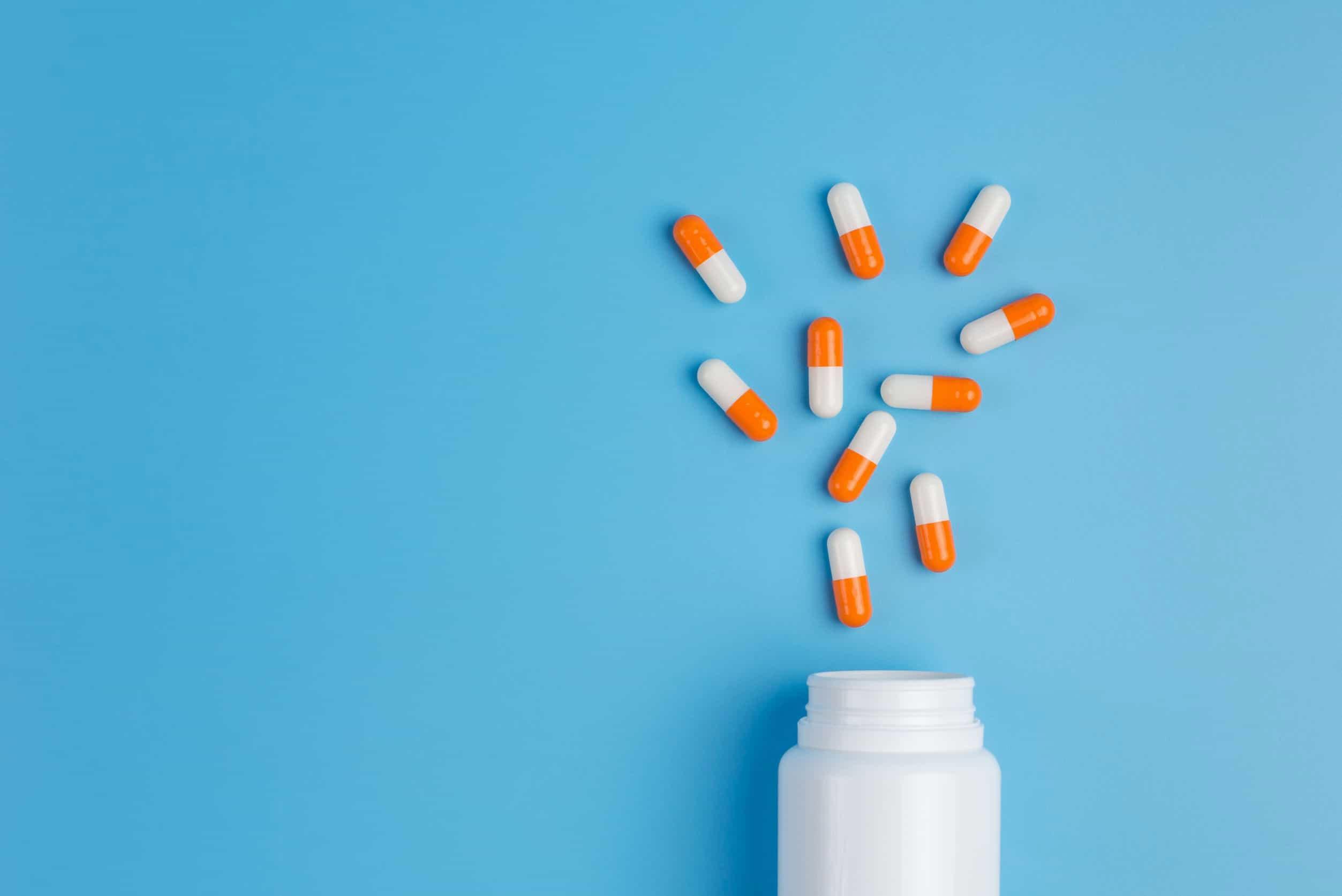 Orange and white pills spilled out of a white bottle on a blue background.