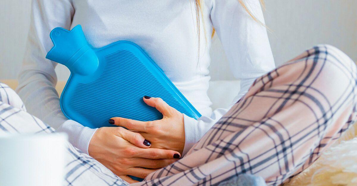 A young woman in her pajamas is holding a hot water bottle to her abdomen.