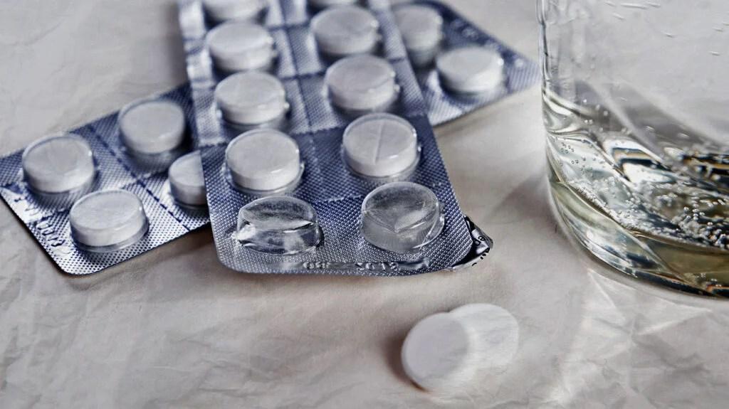 Two blister packs of pills and a glass of water on a white surface.