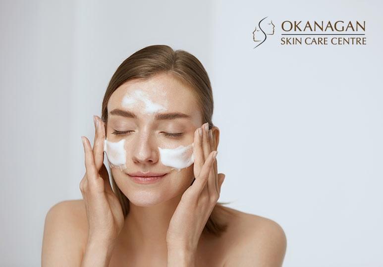 A woman with her eyes closed is washing her face with a foamy cleanser.