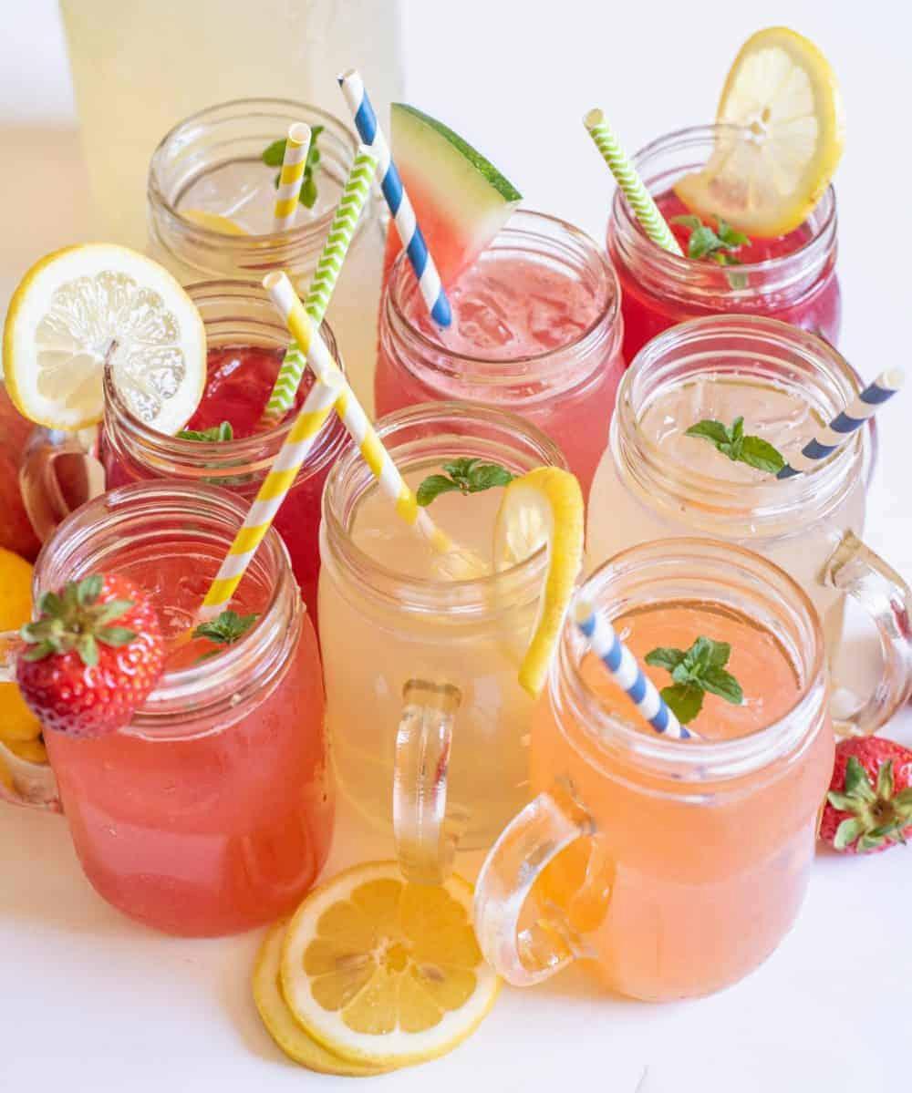 Several glass jars of homemade lemonade in various fruit flavors.