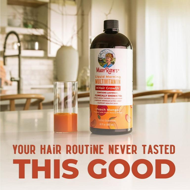 A bottle of Mary Ruths Liquid Morning Multivitamin + Hair Growth supplement sits on a table next to a glass of juice.