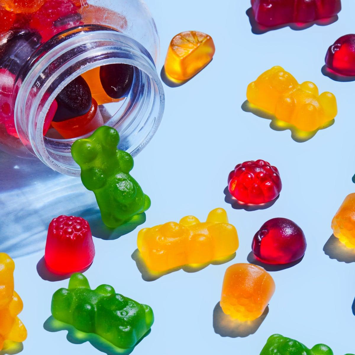 Colorful gummy bears and other fruit-shaped candies spilling out of a clear plastic bottle onto a blue surface.