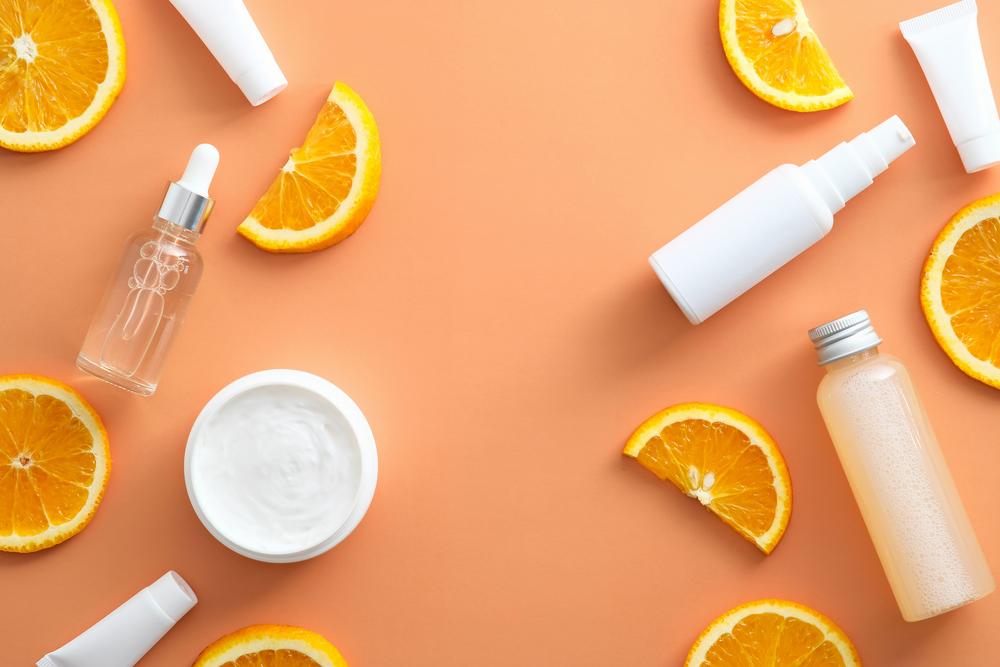 Various skincare products and orange slices are arranged on a solid orange background.