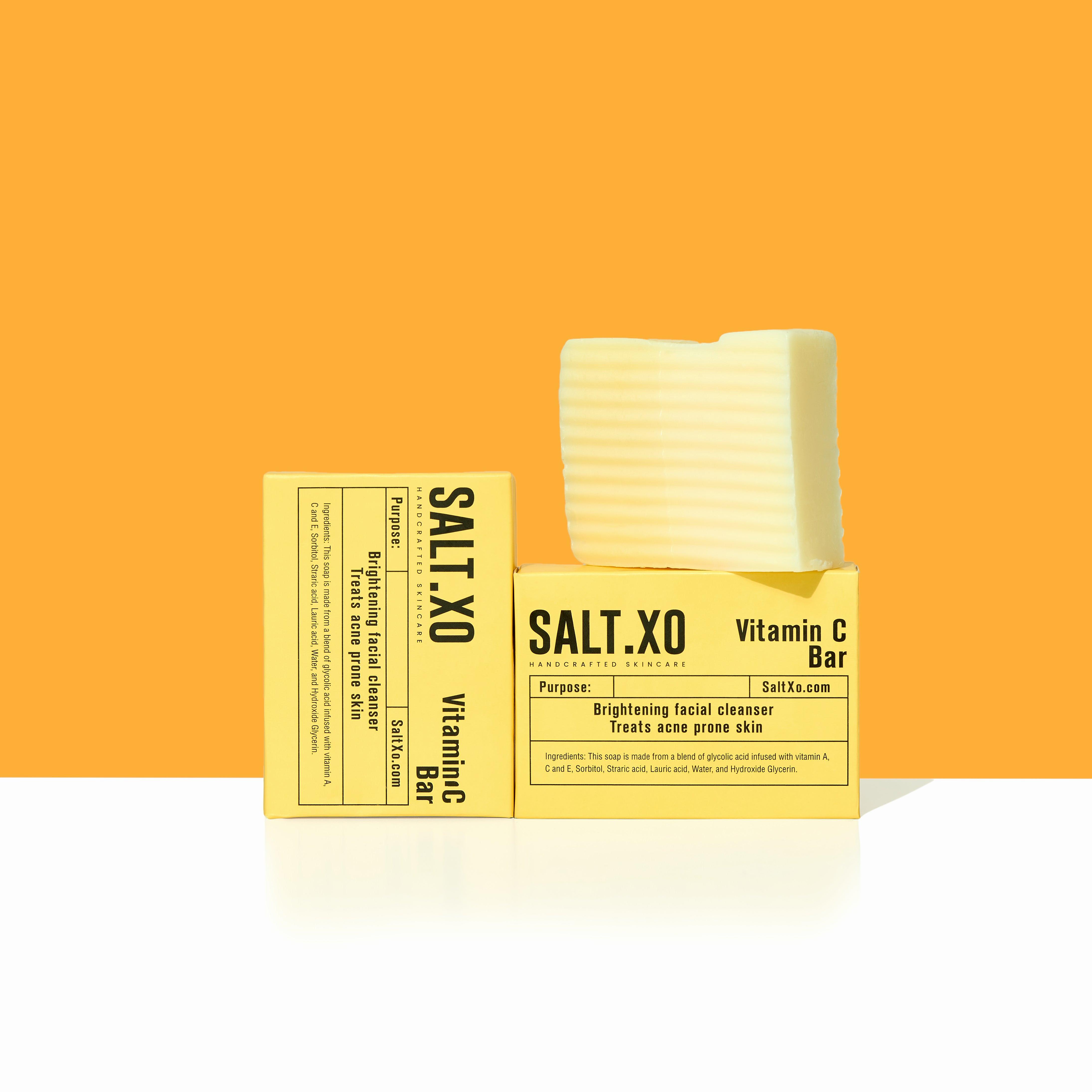 A yellow background displays two white and yellow rectangular boxes of handcrafted skincare products labeled as Vitamin C brightening facial cleanser bars.