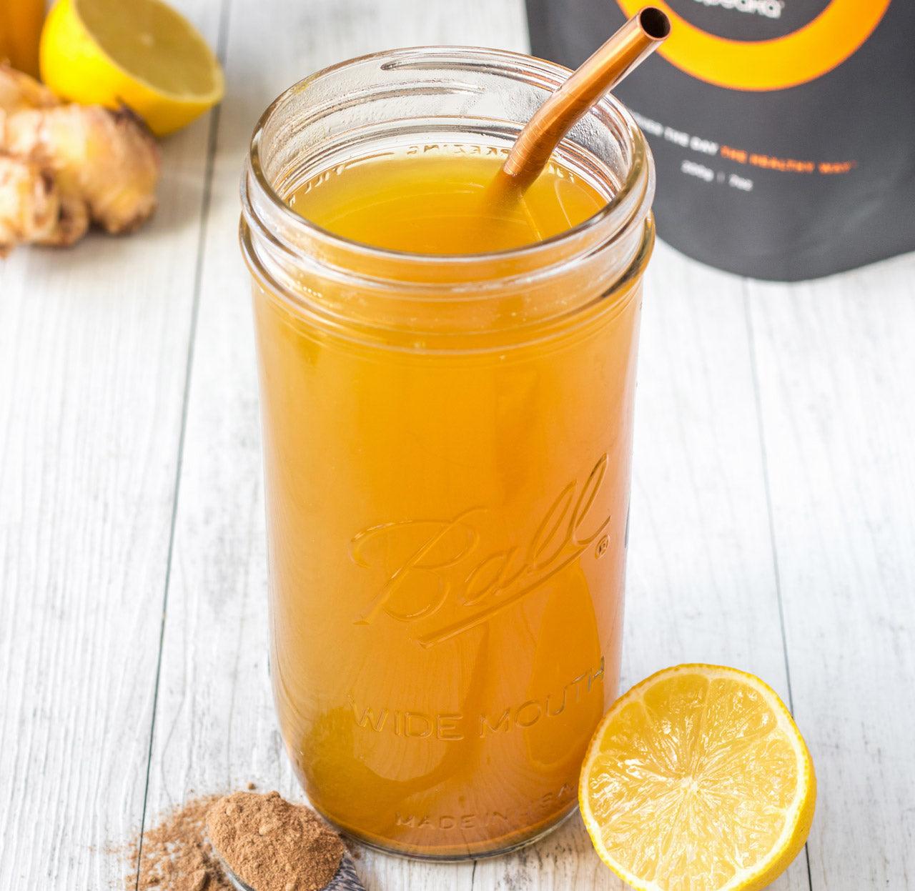 A mason jar of golden turmeric tea sits on a white table, with a lemon wedge and a pile of spice powder next to it.