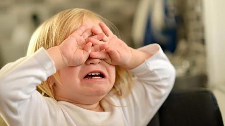 A young child covers their eyes with their hands and cries.