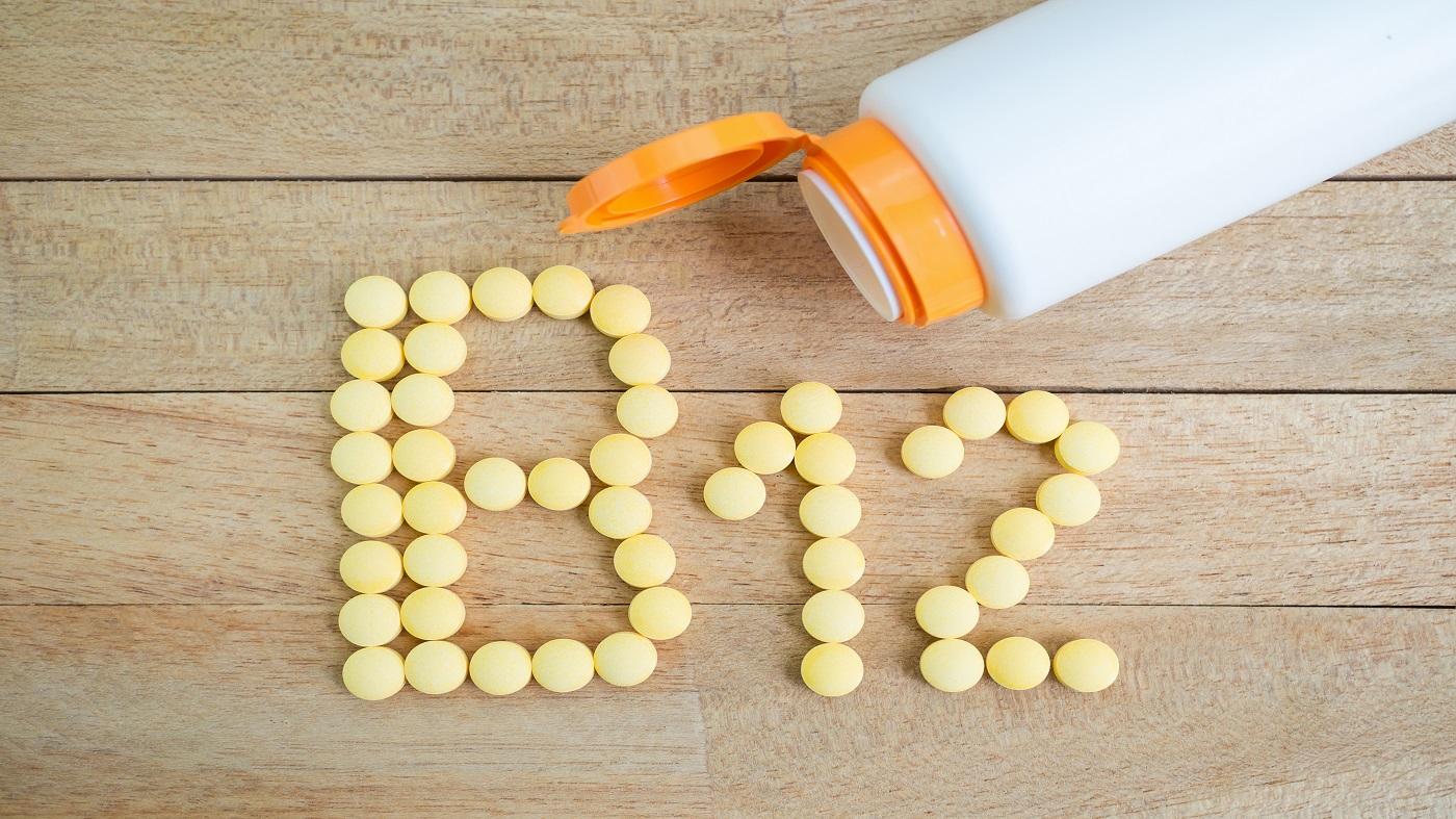 Yellow pills arranged on a wooden table in the shape of the text B12, with an open bottle of pills next to it.