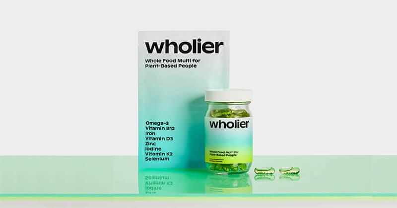 A bottle of Wholier Whole Food Multi for Plant-Based People and two capsules in front of a Wholier box.