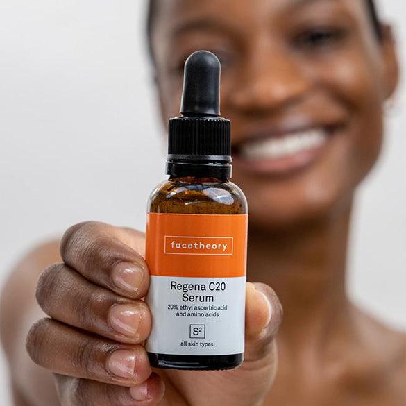 A smiling woman holds up a bottle of Regena C20 Serum.