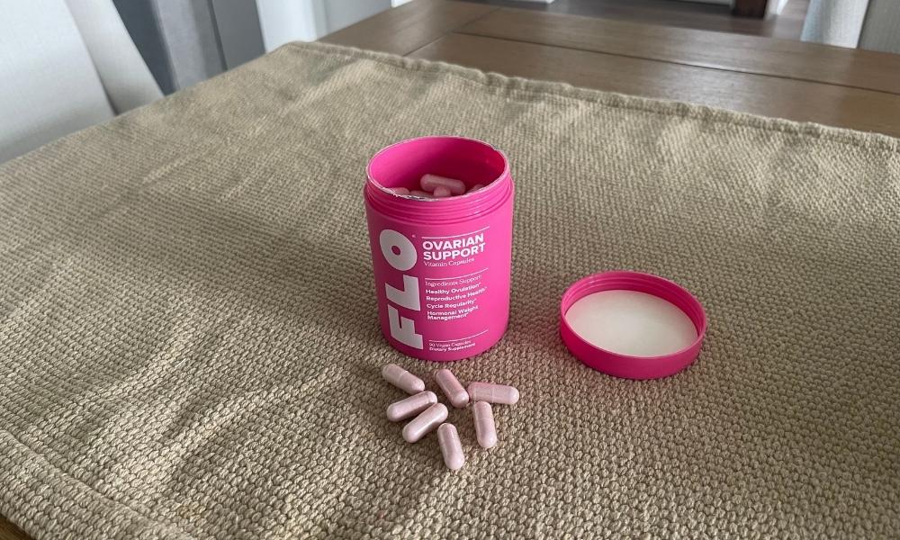 A pink bottle of Flo Ovarian Support capsules next to an open cap and several loose capsules on a cloth napkin.