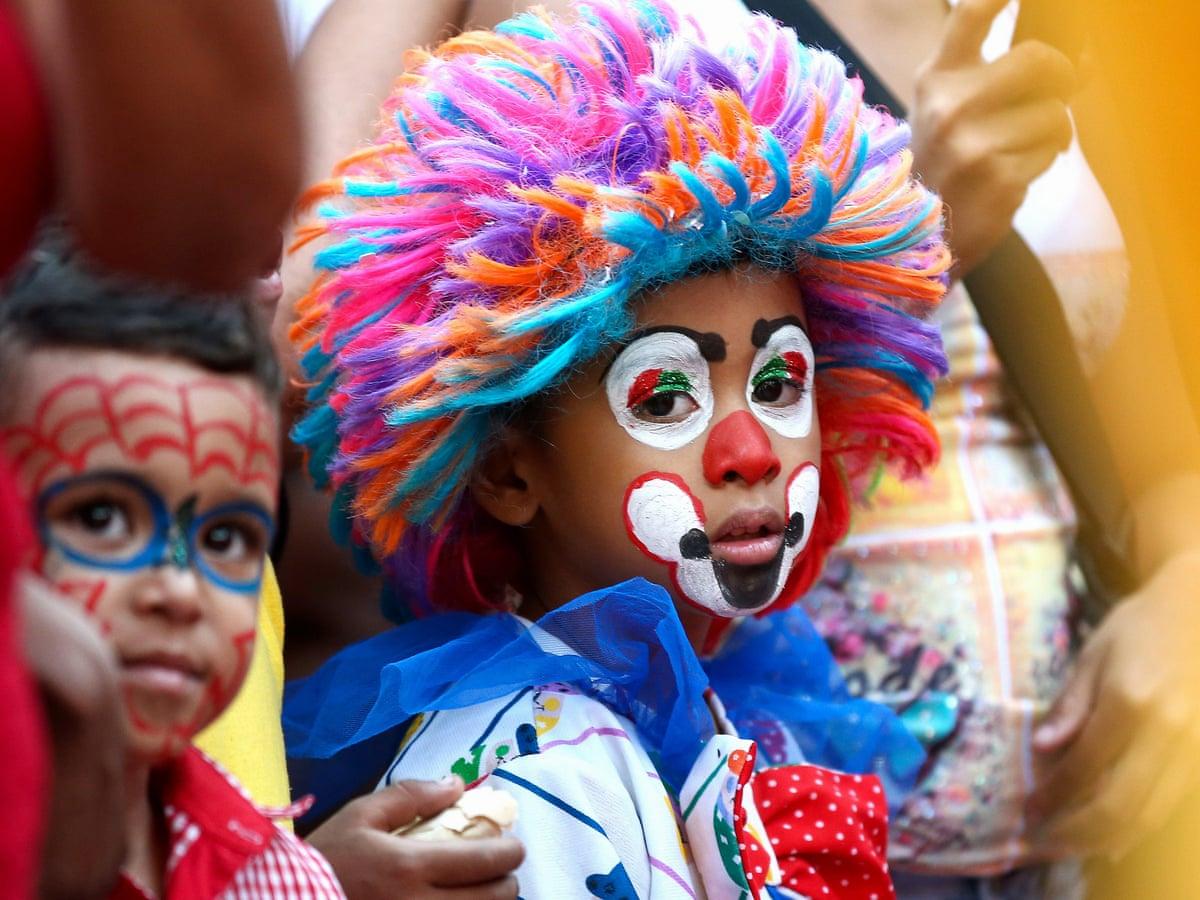 A young boy with face paint and a colorful wig looks on during a festival.