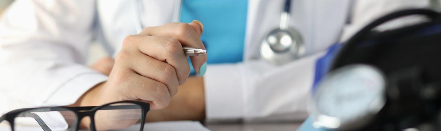 A doctor in a white coat is holding a pen and wearing a stethoscope around their neck.