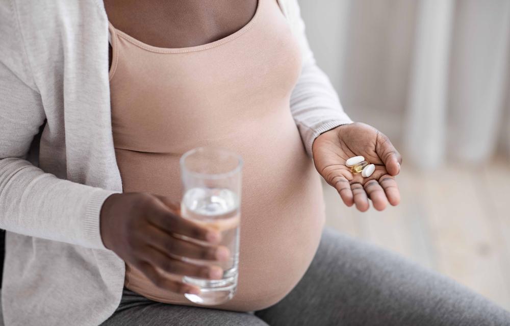 A pregnant woman holding a glass of water in one hand and prenatal vitamins in the other.