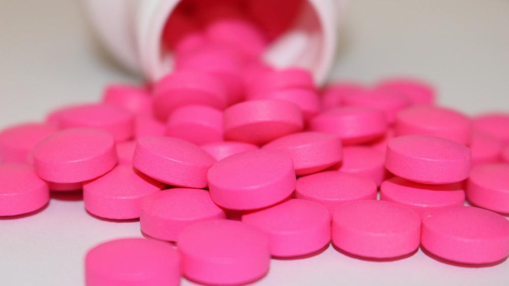 A close-up image of a pile of pink pills that have been spilled from a white bottle.
