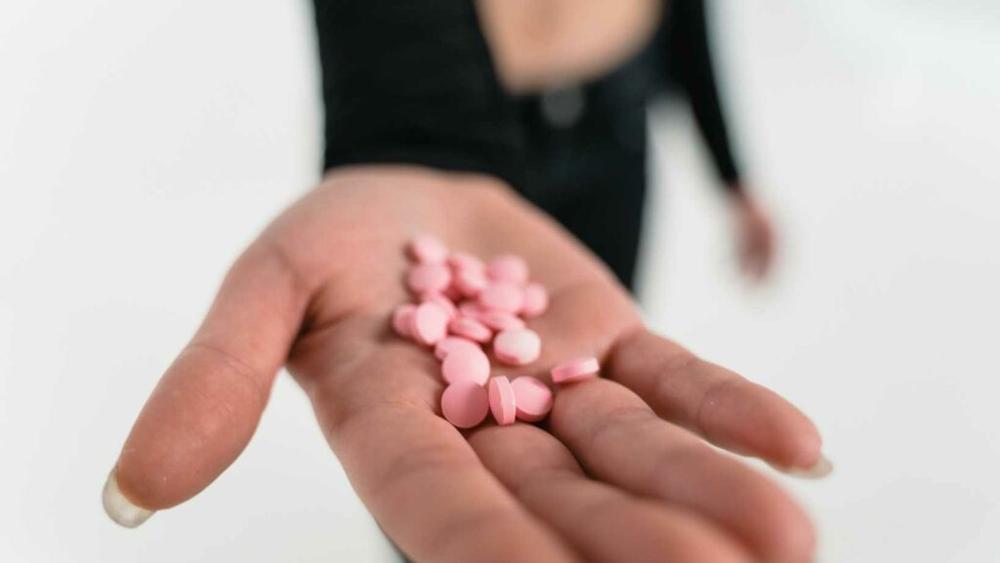 An outstretched hand holding several pink pills.