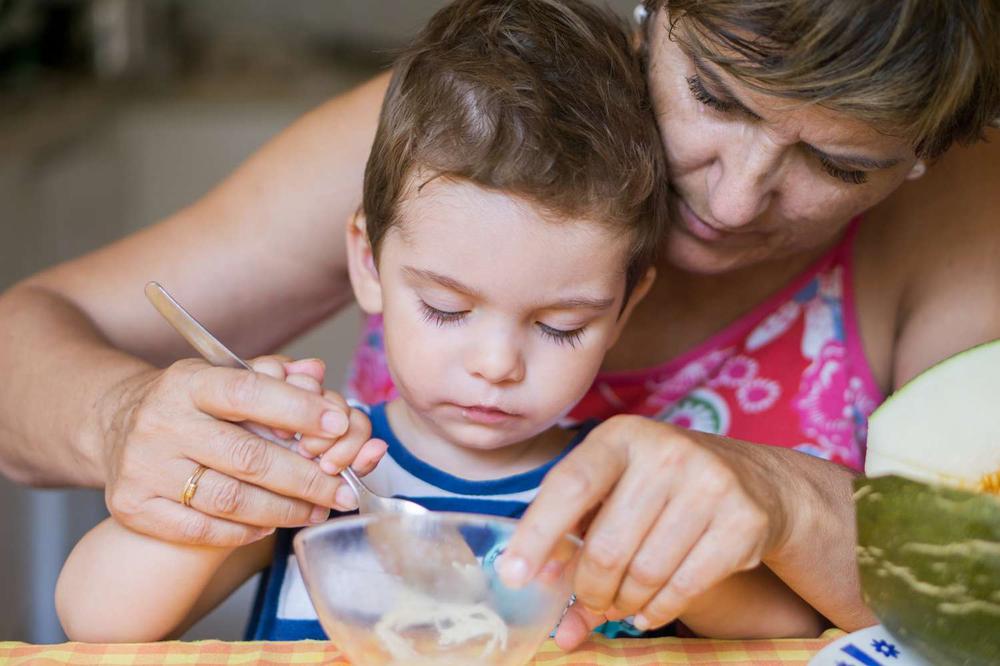 A grandmother is feeding her grandson with a spoon.
