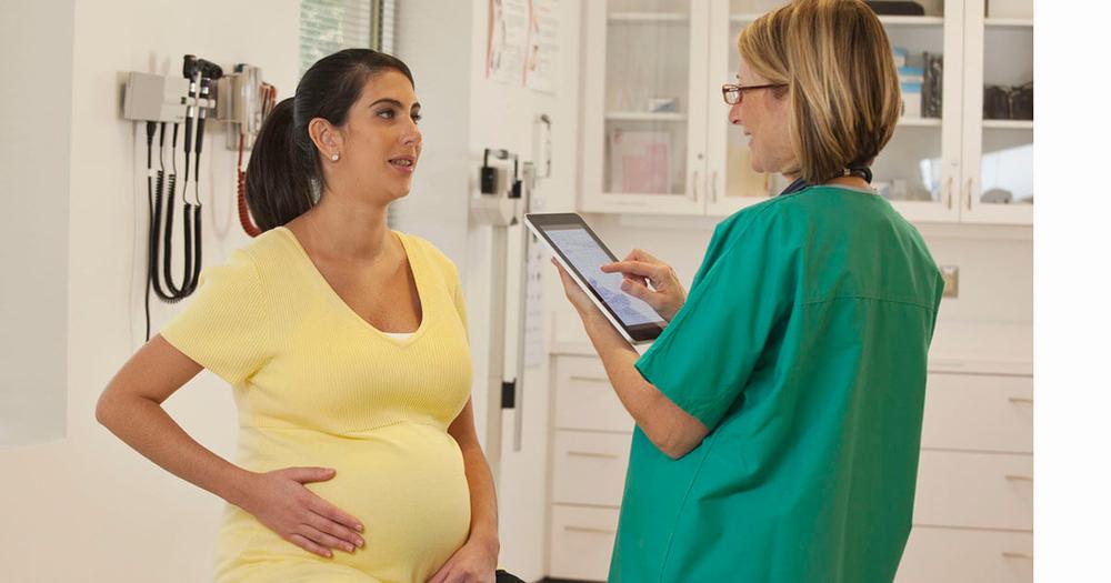 Pregnant woman talking with her doctor while looking at a tablet.