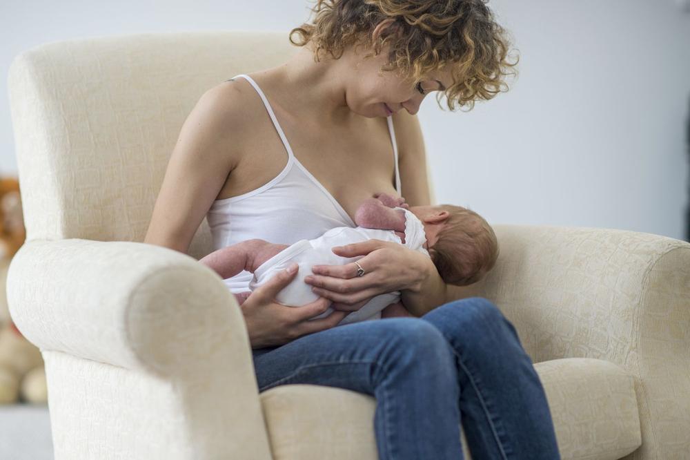 A mother is breastfeeding her newborn baby in a comfortable armchair.