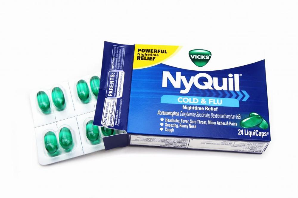 A box of NyQuil Cold & Flu medicine with green pills spilling out of it.
