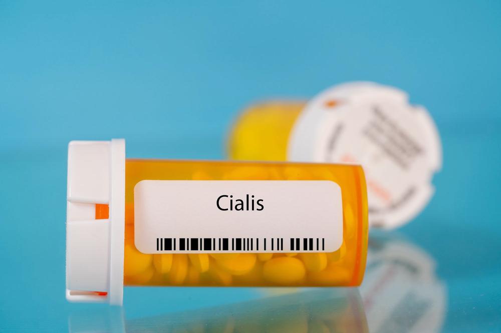 A close-up of a prescription bottle containing yellow pills and labeled Cialis.