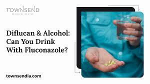 A persons hand holding green and white pills with the text Diflucan & Alcohol: Can You Drink With Fluconazole? next to it.