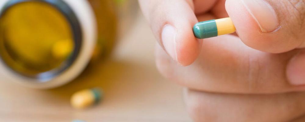 A close-up of a hand holding a green and yellow pill.