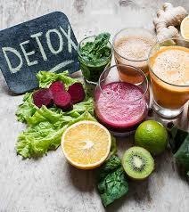 An assortment of fruits and vegetables are arranged on a table with a chalkboard sign that says detox written on it.