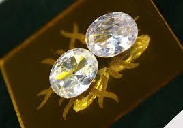 Two oval diamonds sit on a reflective surface.