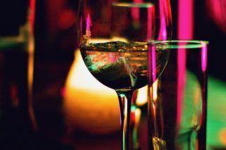 Close-up of a glass of white wine, with the glass illuminated with pink and green light.