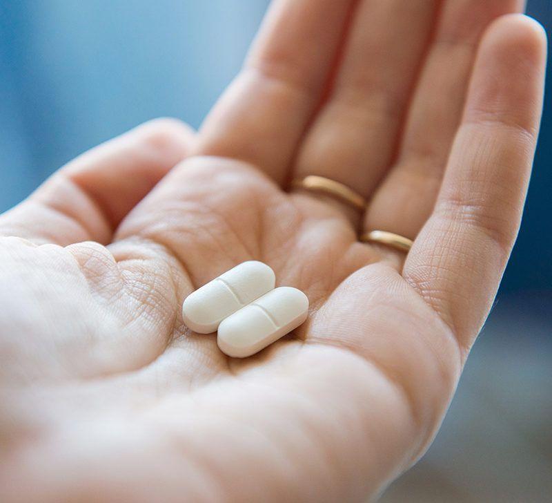 Two white pills in the palm of a persons hand.