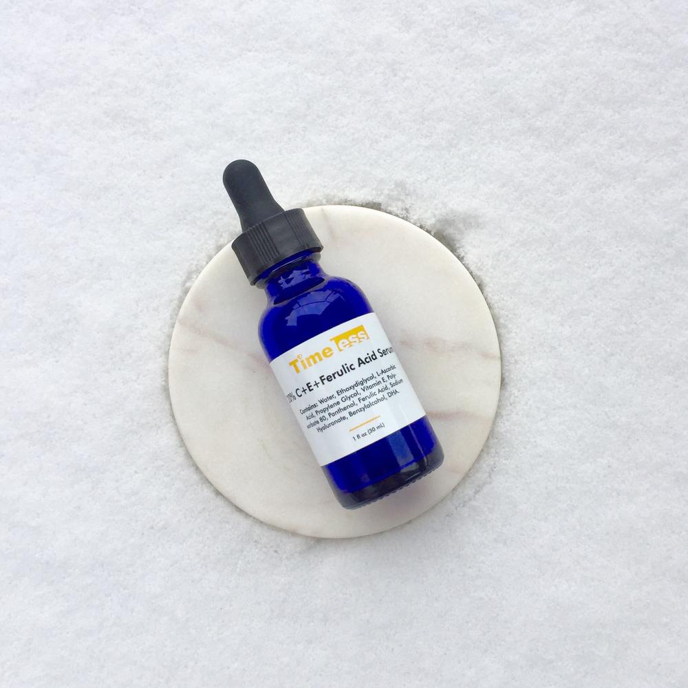 A blue glass bottle of Time less C+E+Ferulic Acid Serum sits on a white marble slab.