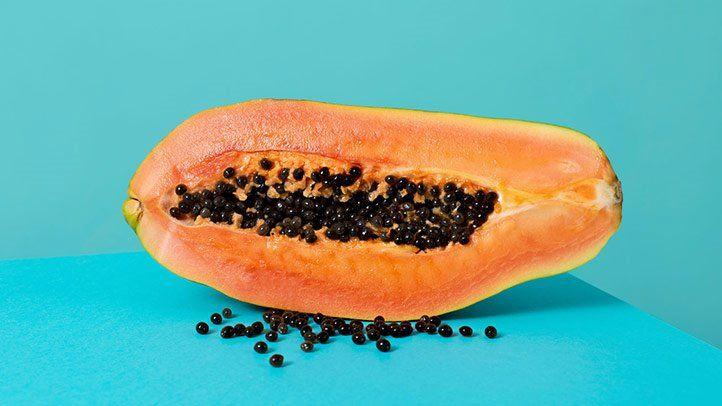 A halved papaya on a blue background with some seeds scattered around it.