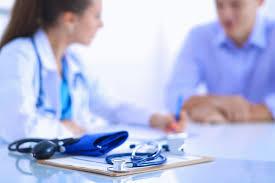 A stethoscope and blood pressure cuff rest on a table in front of a doctor and patient.