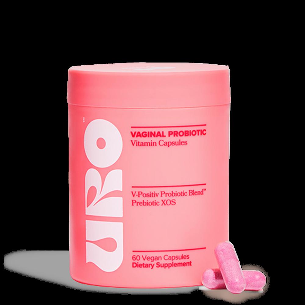 A pink bottle of VURO vaginal probiotic vitamin capsules with two pink capsules next to it.