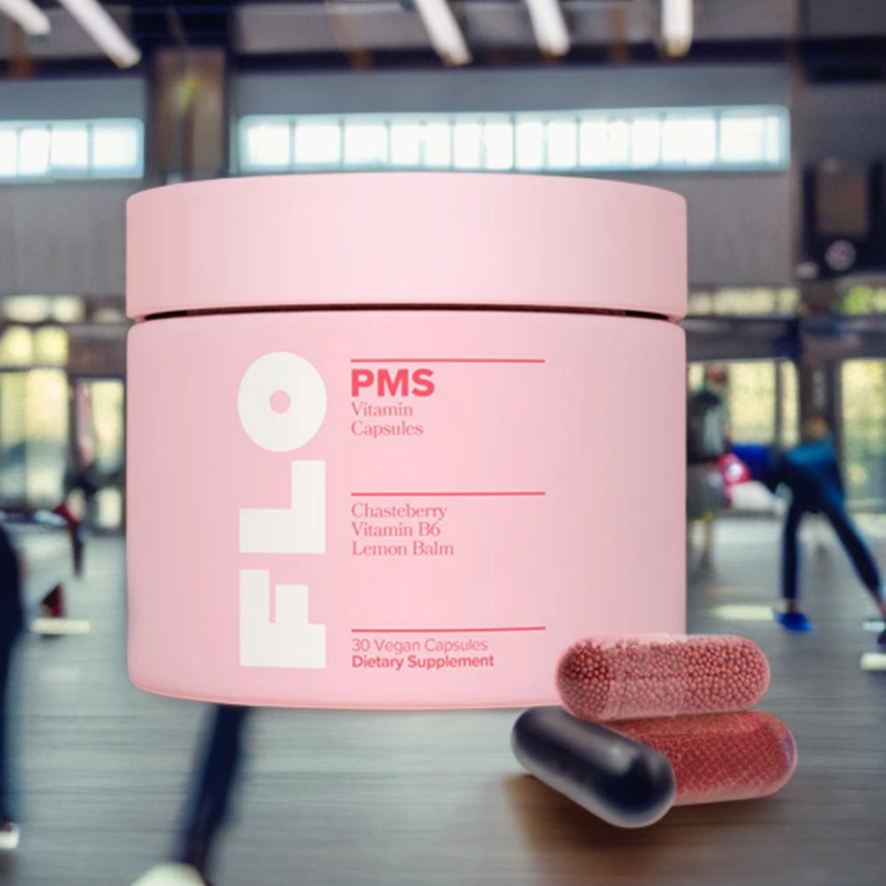 A pink bottle of Flo PMS Vitamin Capsules with two black and red capsules in front of it.