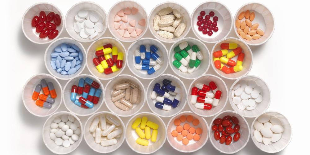A variety of pills and capsules in white paper cups.