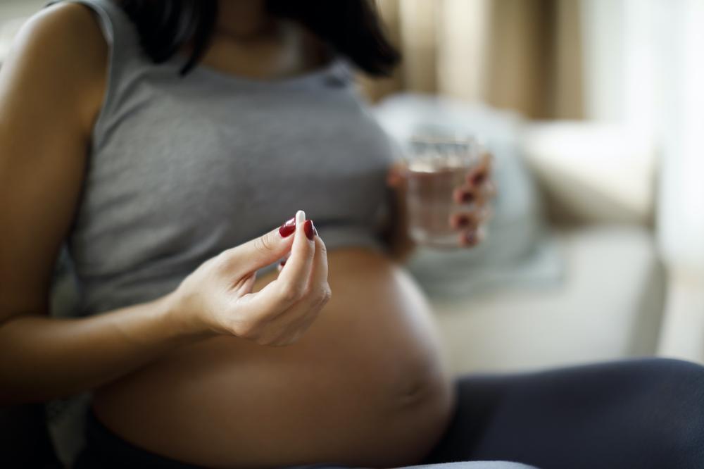 A pregnant woman is holding a pill in her hand and a glass of water.