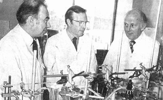 Three scientists in lab coats are working on an early model of the artificial kidney.